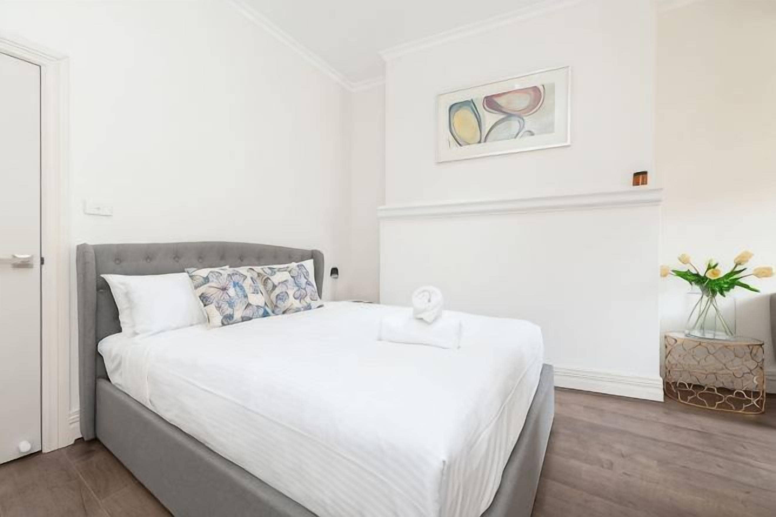 Una cama bien hecha con cabecera gris, ropa de cama blanca y una sola almohada.