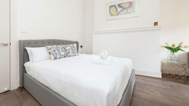 A neatly made bed with a grey headboard, white bedding, and a single pillow. - Stunning Sydney Home 9 (Millers Point)