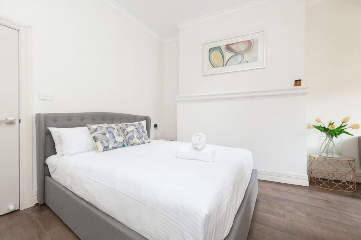 A neatly made bed with a grey headboard, white bedding, and a single pillow.