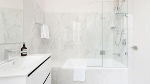 A modern bathroom with a glass-enclosed shower, a white sink, and marble walls. - Stunning Sydney Home 9 (Millers Point)