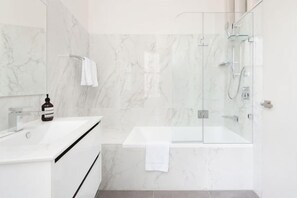 A modern bathroom with a glass-enclosed shower, a white sink, and marble walls. - Stunning Sydney Home 9 (Millers Point)