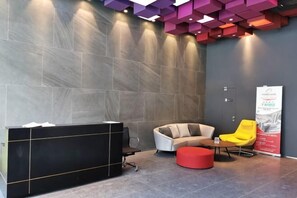 A reception area with a black reception desk, a grey sofa, a yellow chair, and a red ottoman.