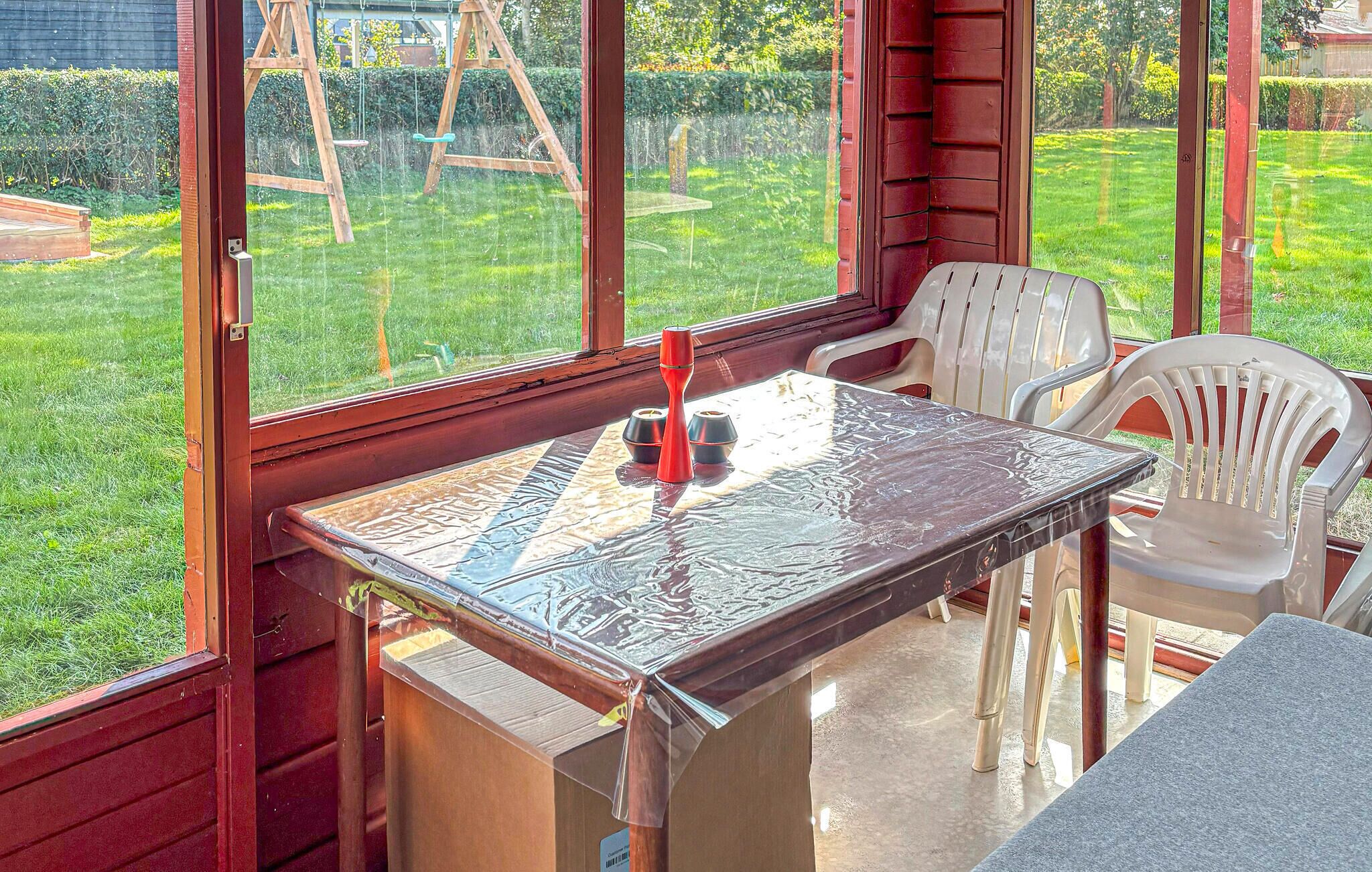 Een zonnige kamer met een tafel en stoelen, grote ramen en uitzicht op een tuin.