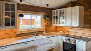 A kitchen with wooden walls, a window, cabinets, a sink, a stove, and a chair. - 3 bedroom beautiful home in Haderslev (Haderslev)