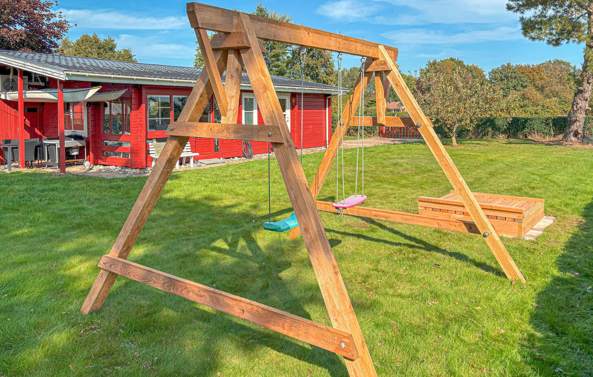 Een houten schommel in een gazon met een rood gebouw op de achtergrond.