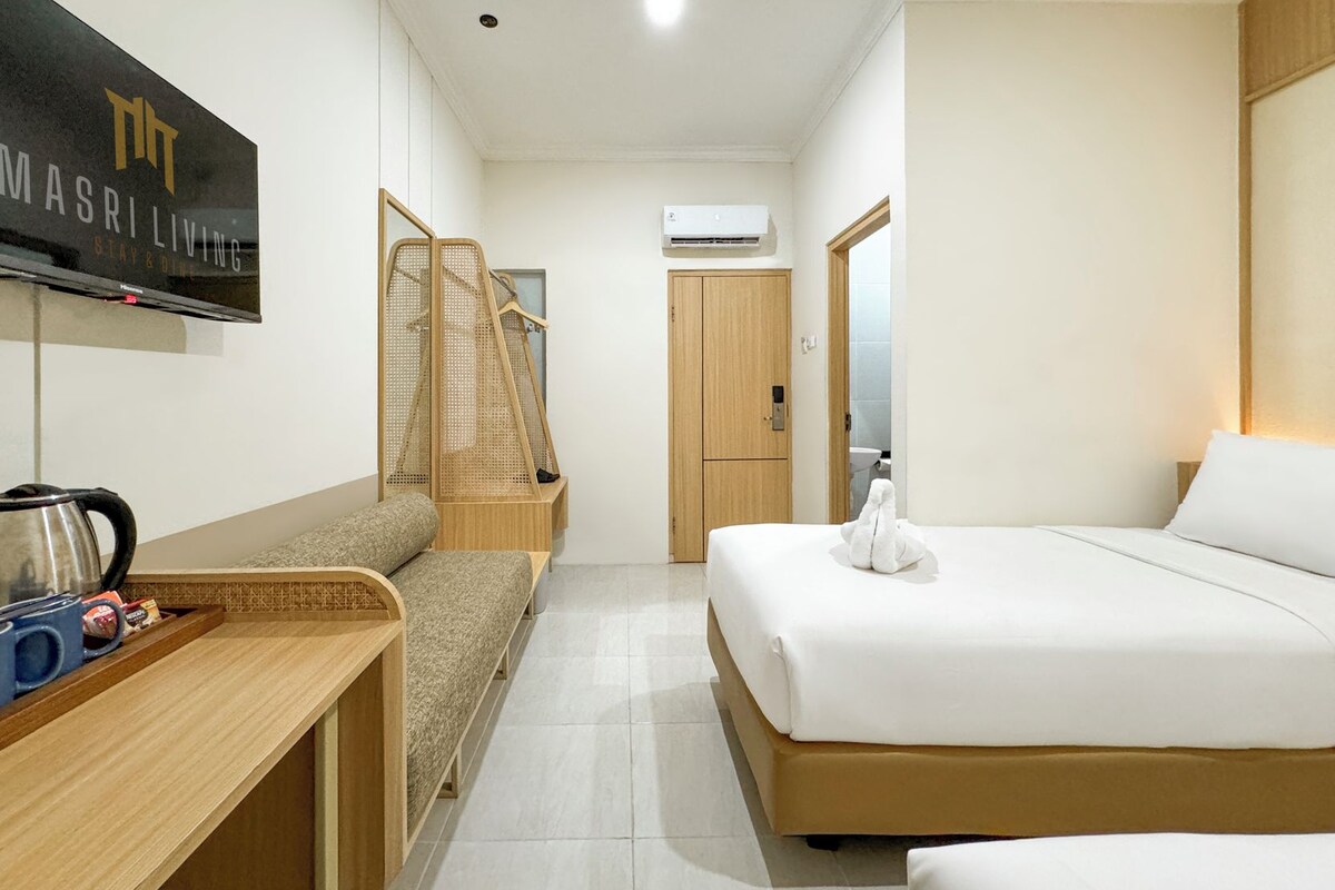 A hotel room with a bed, a sofa, a TV, a coffee maker, and a wooden wardrobe.