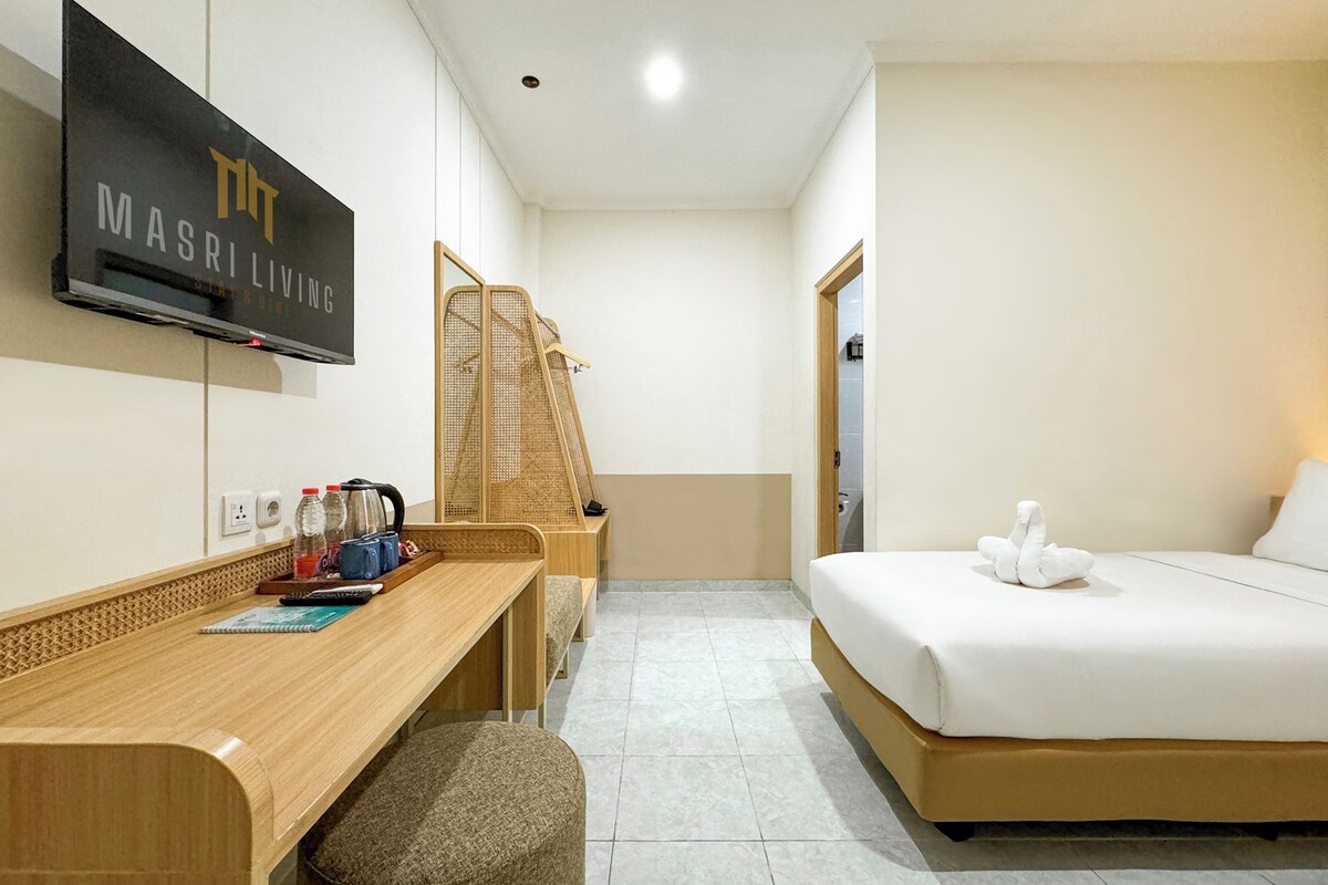 A hotel room with a bed, a desk with a chair, a television mounted on the wall, and a wooden wardrobe.