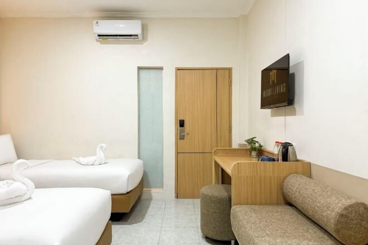A hotel room with two beds, a desk, a sofa, an air conditioner, and a TV.
