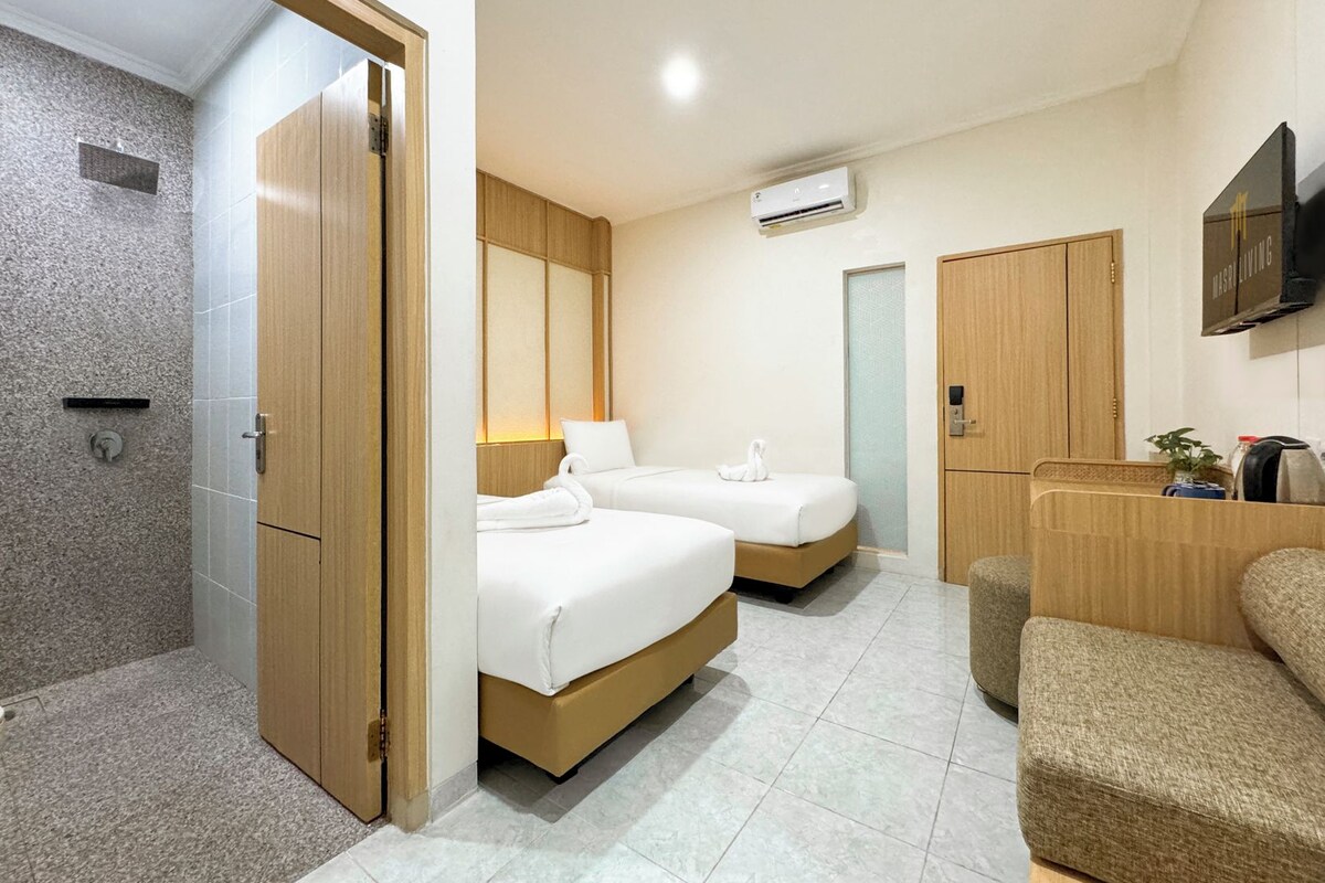 A hotel room with two beds, a shower area, a seating area, and a mounted television.