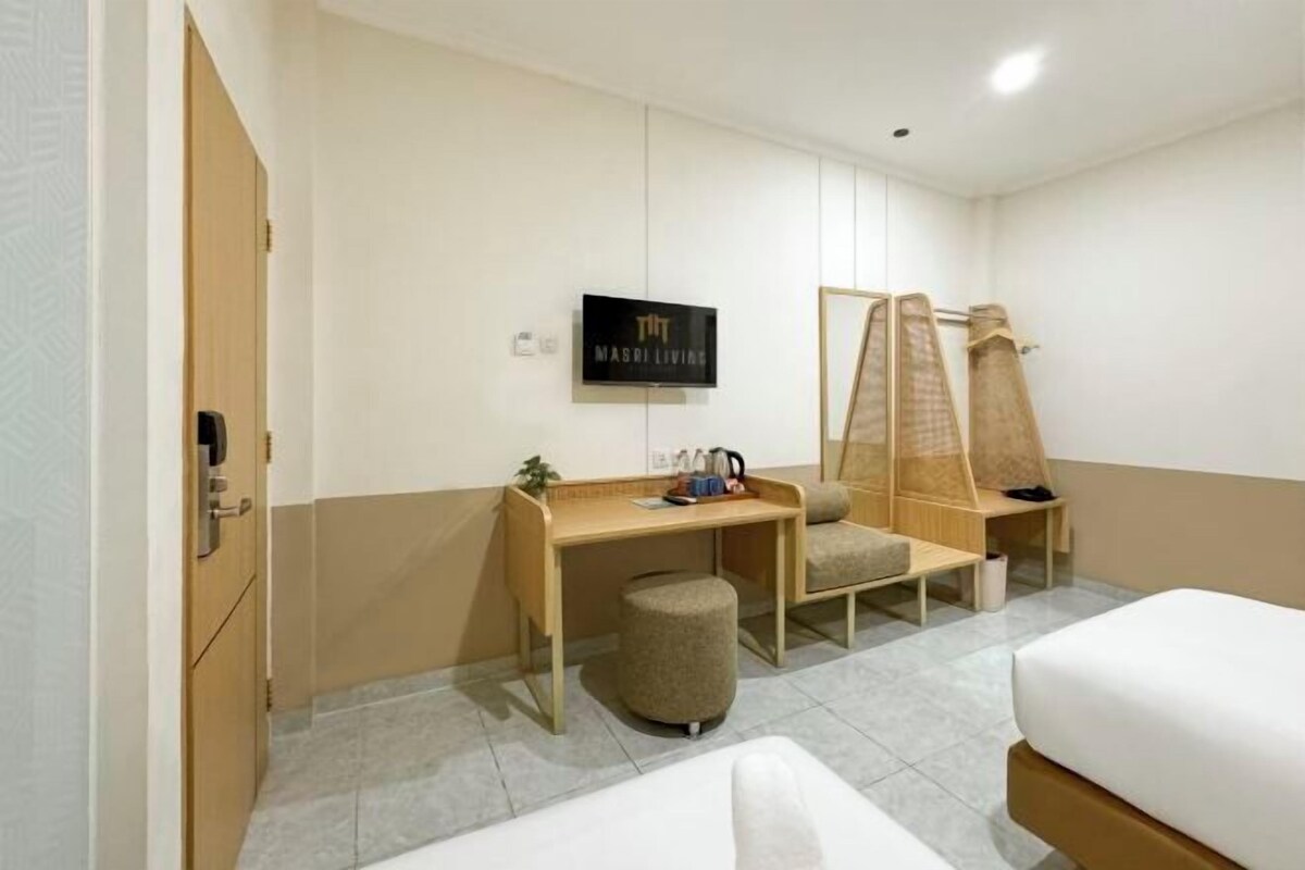 A hotel room with a bed, a desk, a chair, a small stool, a TV, and a wall-mounted shelf.