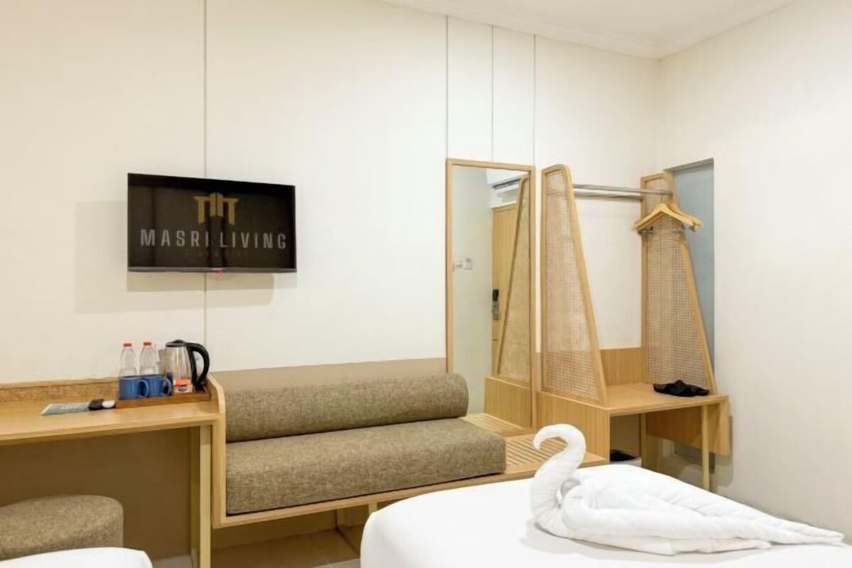 Une chambre d’hôtel comprenant un lit, un canapé, une télévision, un miroir, une armoire et un bureau en bois avec une bouilloire et des bouteilles.
