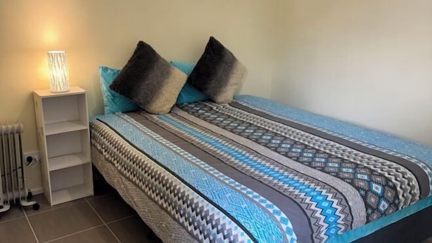 Ein Schlafzimmer mit einem Bett, Kissen, einem Nachttisch und einer Lampe.