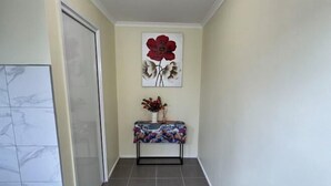 Ein Korridor mit einer Tür links, einem Wandbild einer roten Blume und einem kleinen Tisch mit Blumen.'