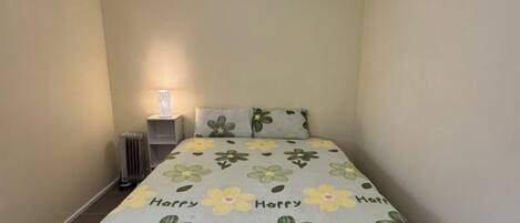 A small, single-bed room with a floral bedspread, a bedside lamp, and a radiator.