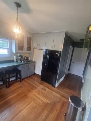 Une cuisine avec un plancher en bois, un réfrigérateur noir et des armoires blanches.