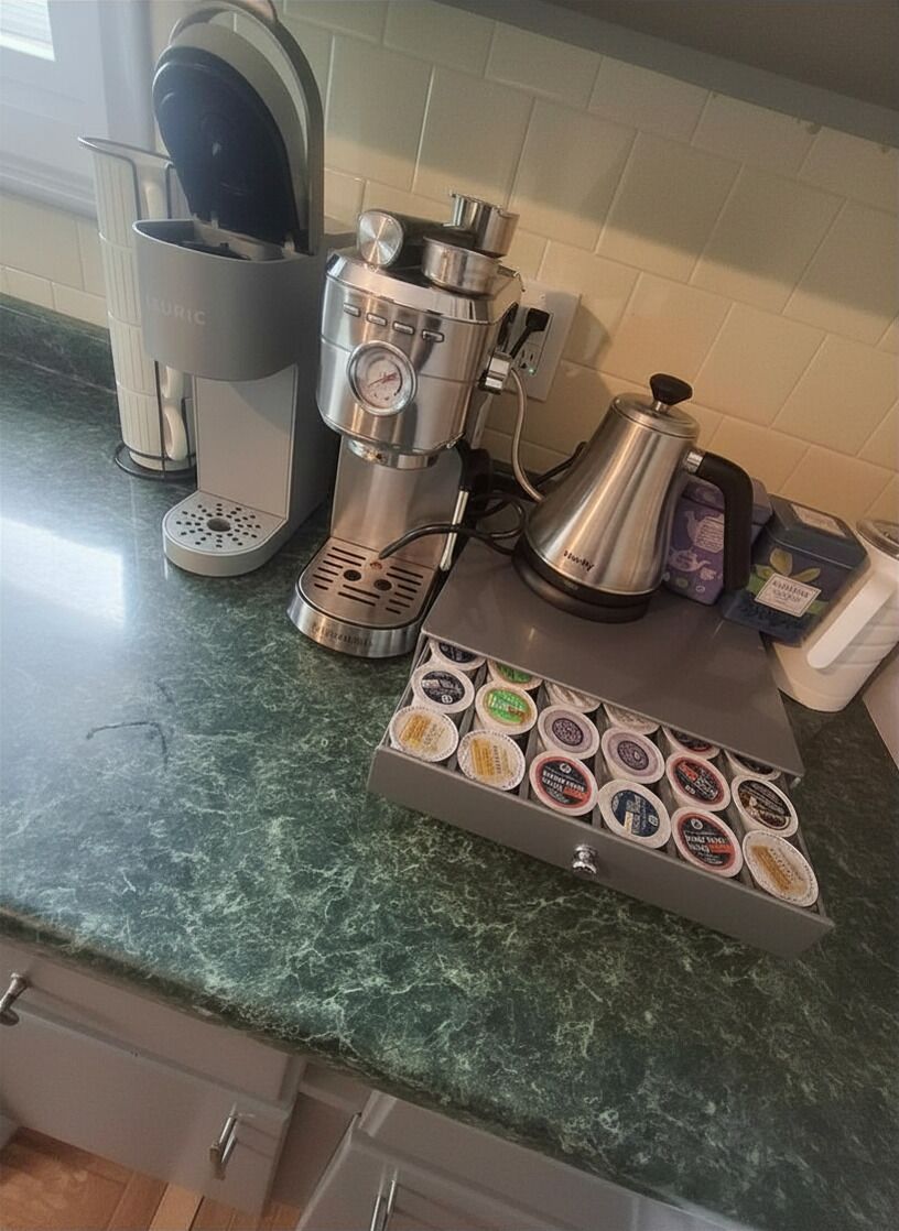 A kitchen with a coffee maker, a kettle, and a coffee pod holder.