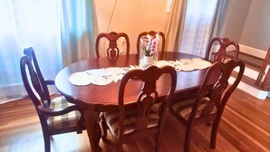 Un comedor con una mesa redonda, seis sillas, una araña y una ventana con cortinas.