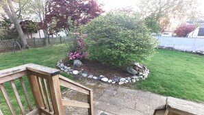 Una terraza de madera con un sendero de piedra que conduce a un jardín con un pequeño arbusto y flores rosas.