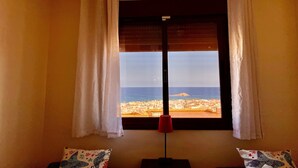 Ein Zimmer mit großem Fenster, weißen Vorhängen, einer roten Stehlampe und gemusterten Kissen.