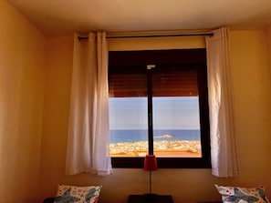 A room with a large window, white curtains, a red floor lamp, and patterned pillows.