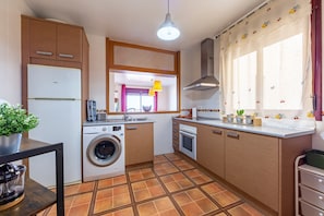 Une cuisine de taille réduite équipée d’un lave-linge, d’un four et d’une fenêtre avec des rideaux.