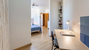 Ein modernes Zimmer mit einem Holztisch, einem Sessel, einem Bett, einem Bücherregal und einem Deckenventilator.