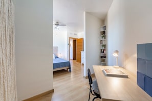 A modern room with a wooden desk, a chair, a bed, a bookshelf, and a ceiling fan.