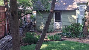Un edificio residenziale con facciata verde, un patio in legno e un giardino curato con diverse piante.