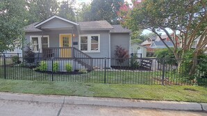 Una casa a un piano con portico, un piccolo giardino e una recinzione in metallo nero.