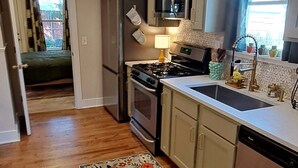 Una cucina con pavimento in legno, un tappeto floreale, elettrodomestici in acciaio inossidabile e una finestra con tende.