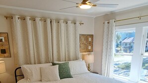 Una camera da letto con un letto grande, un ventilatore a soffitto e una finestra con tende.