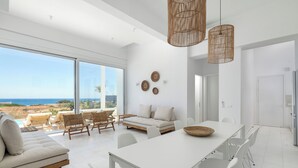 Un interior moderno con zona de comedor blanca, sofá y vista al océano.