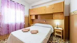 A bedroom with a bed, wooden cabinets, a nightstand, a lamp, and a patterned floor. - Holiday Home 'Mirador De Sorbas' with Balcony and Air Conditioning (Carboneras)