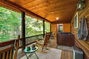 Eine Holzhütte mit Veranda, Schaukelstühlen, einem Tisch und Blick auf den Wald.