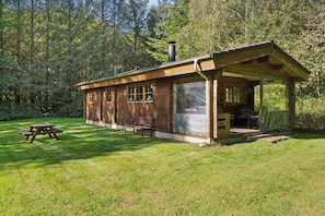 Une cabane en bois dotée d’un porche couvert, d’une table de pique-nique et d’un banc, située dans une zone boisée.