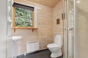 A wooden cabin bathroom with a window, a sink, a toilet, and a shower.