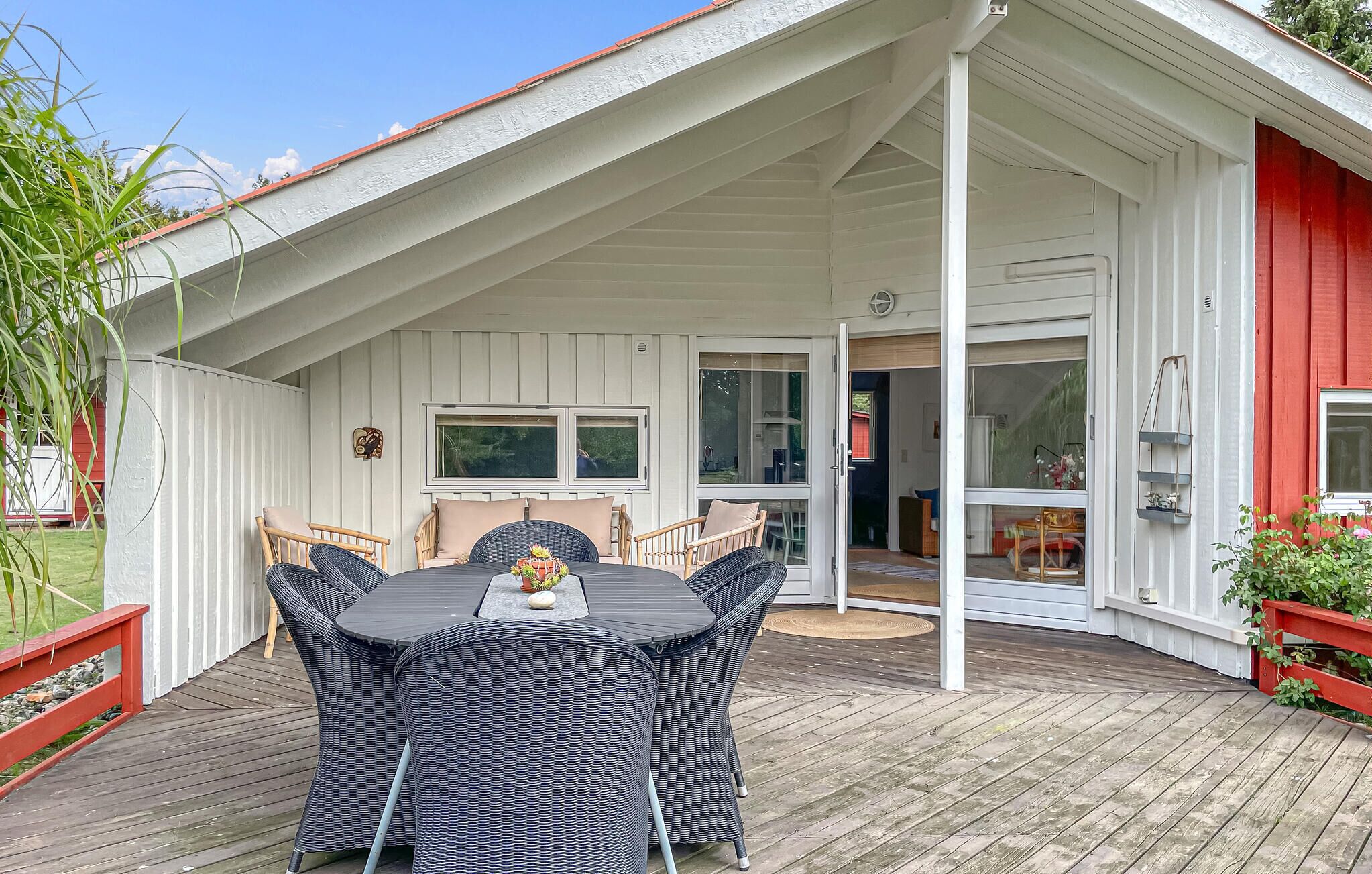 A covered patio with a dining table and chairs, a red and white building, and a wooden deck.
