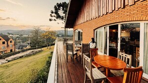 A wooden deck with a table and chairs, overlooking a grassy area and buildings in the distance.