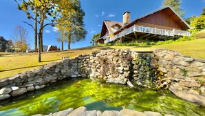 A rustic cabin with a stone bridge leading to a pond.