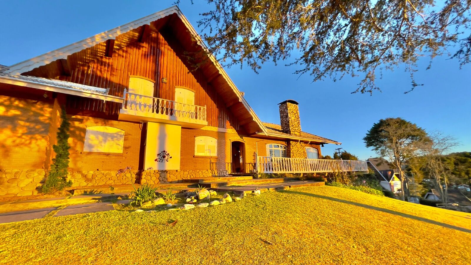Une maison en bois avec une cheminée en pierre, un balcon et une pelouse bien entretenue.