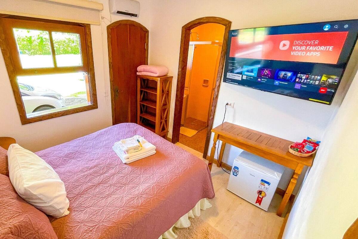 Ein Schlafzimmer mit einem Bett, einem an der Wand montierten Fernseher, einem Fenster und einer Tür.