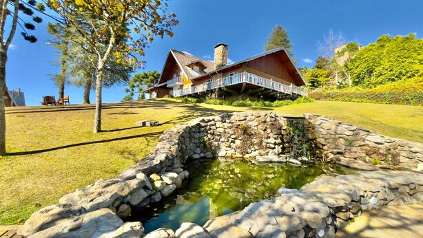 A rustic cabin with a stone pond in the foreground, surrounded by a well-maintained lawn and trees.