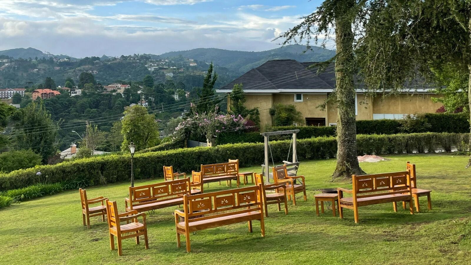 A grassy outdoor area with wooden benches and a swing set, surrounded by well-maintained hedges and trees.