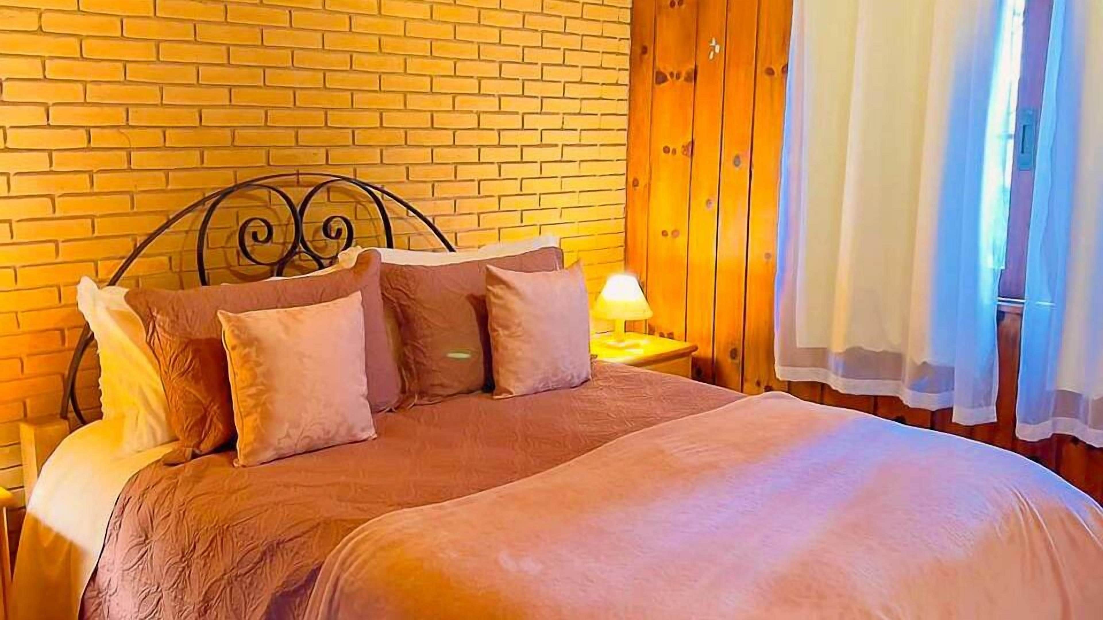 A bedroom with a brick wall, wooden paneling, a metal bed frame, and a bedside lamp.
