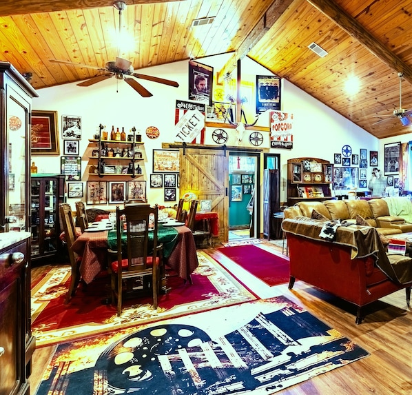 A cozy, rustic interior with a dining area, a living room with a leather sofa, and a ceiling fan. - Here ye, Here ye! Royal Retreat 5 Minutes to Scarborough Renaissance Festival! (Waxahachie)