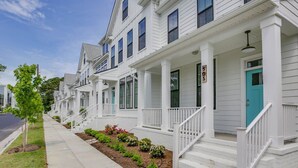 A row of white townhouses with front porches, numbered signs, and a clear sidewalk. - Beachside 4BR Home • Walk to Boardwalk & Atlantic Park (Virginia Beach)