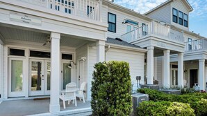 A two-story house with a covered porch, white exterior, and a small garden area. - Beachside 4BR Home • Walk to Boardwalk & Atlantic Park (Virginia Beach)