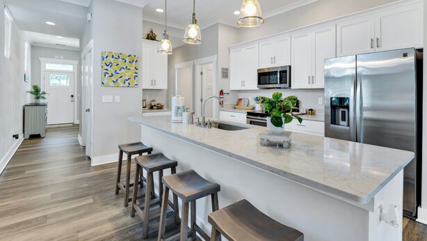A modern kitchen with white cabinets, a stainless steel refrigerator, and a central island with bar stools. - Beachside 4BR Home • Walk to Boardwalk & Atlantic Park (Virginia Beach)