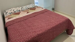 Una cama con una colcha roja estampada con flores y un edredón de diseño geométrico.