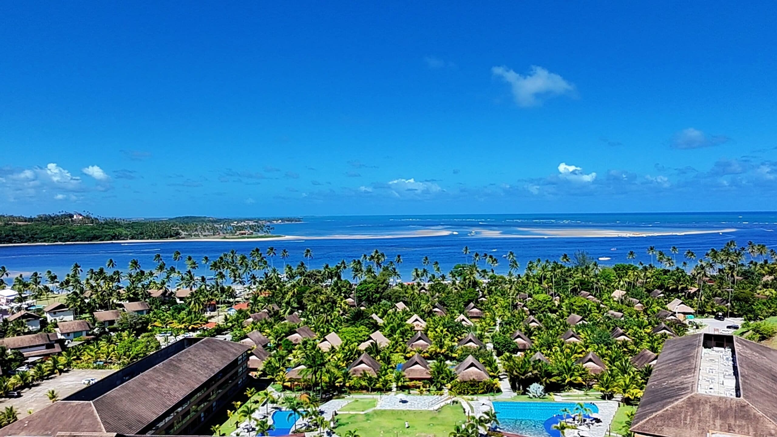 Un resort con bungalows de techo de paja, una piscina y vistas al océano.